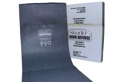 A roll of grey protective material with the Skudo logo is partially unrolled in front of a branded box. Keywords: protection, Skudo Door Defense.