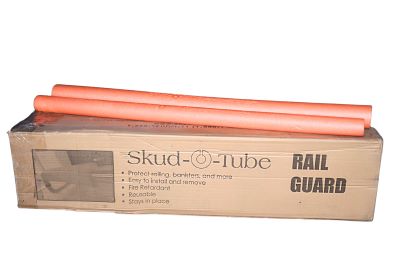 Cardboard box labeled "Skud-O-Tube Rail Guard" with safety features listed. Two orange tubes are stacked on top, suggesting protective equipment.