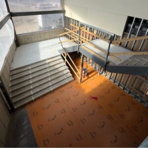 a open corridor and stairwell under construction with the stairs protected by grey fitting material and flooring protected with an orange mat.